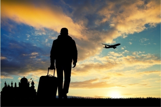 silhouette of man with luggage walking into sunset; mosque to the left of picture